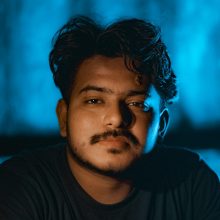 Close-up portrait of a young man with a thoughtful expression against a blue backdrop.